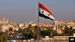 A Syrian national flag waves as vehicles move slowly on a bridge during rush hour, in Damascus, Syria, Feb. 28, 2016.