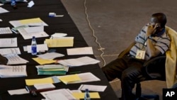 A tired election worker sits to make a phone call surrounded by his papers at the National Tallying Center.