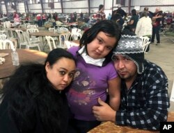 Wildfire survivors, Marolyn Romero-Sim, left, with Hugo Romero-Rodriguez and their 9-year-old daughter, Milagros, sit inside the evacuation center at the Ventura County Fairgrounds in Ventura, Calif. Their RV burned up with all their possessions.