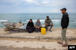 People sit by a beached boat along the Mediterranean seashore at the Shati camp for Palestinian refugees north of Gaza City on Feb. 11, 2025.