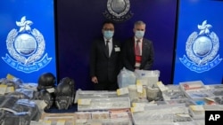 Senior Superintendent Li Kwai-wah, left, of Hong Kong Police National Security Department, and senior bomb disposal officer Alick McWhirter, right of Explosive Ordnance Disposal Bureau, pose with the confiscated evidence during a news conference.