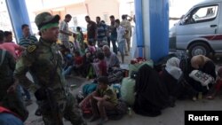 An Iraqi Shi'ite fighter walks with his weapon past internally displaced Sunni people fleeing the violence in the city of Ramadi at the outskirts of Baghdad, May 19, 2015. 