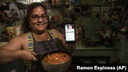 Contributor Yuliet Colon poses for a photo holding a pot of her creation, “Cuban-style pisto manchego," and her phone that displays the Facebook page, “Recipes from the Heart,” in her home in Havana, Cuba, Friday, April 2, 2021.(AP Photo/Ramon Espinosa)