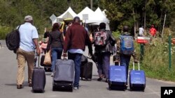A family from Haiti approaches a tent in Saint-Bernard-de-Lacolle, Quebec, stationed by Royal Canadian Mounted Police, as they haul their luggage down Roxham Road in Champlain, N.Y., Aug. 7, 2017.