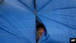 ARCHIVO - Un niño asoma la cabeza desde el interior de una tienda improvisada en la ribera del río Grande, en Matamoros, México, en mayo de 2023.