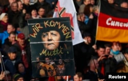 FILE - Supporters of the anti-Islam movement PEDIGA hold a poster depicting German Chancellor Angela Merkel with text reading "We are coming, mommy!" during a demonstration in Dresden, Germany, Feb. 6, 2016.