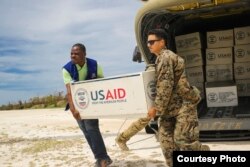 FILE - Cpl. Steven Arroyo, a heavy equipment mechanic with Marine Wing Support Detachment 31, aids an International Organization for Migration representative in carrying supplies at Jeremie, Haiti, Oct. 9, 2016. (U.S. Marine Corps photo by Cpl. Samuel Guerra/Released)