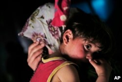 FILE - Syrian refugee child Maria al-Ali, 2, is carried by her mother Huda al-Ali, in the commercial space that the family has rented to live in the city of Gaziantep, southeastern Turkey.