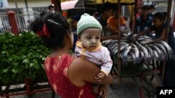A child is carried next to carts with vegetables and fish being distributed during a 'Donate your extras, take what you need' donation drive aimed at helping low-income households in Yangon, Myanmar, on April 6, 2021.