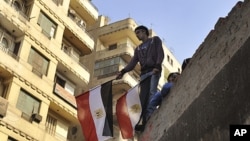 A young Egyptian man holds a national flag while standing on a rooftop between Tahrir Square and the Interior Ministry in Cairo, Egypt, Nov. 26, 2011.