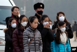 FILE - Young tourists wear masks as they stand near a Chinese Paramilitary policeman in Tiananmen Square in Beijing, China, Dec. 19, 2015.
