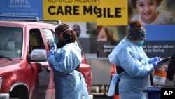 FILE - Critical care nurse Molly Spaeny, left, with St. Vincent Healthcare, speaks with a patient after administering a coronavirus test in a drive-through center in Billings, Mont., March 20, 2020. A test that yields faster results is now on the way.