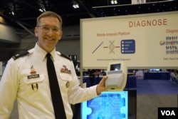 Dr. Matt Hepburn displays a portable diagnostic device for rapid testing of infectious diseases. Trained laboratory workers aren’t needed, and treatment can begin immediately, instead of waiting for results from a faraway lab. (Credit: Art Chimes/VOA)