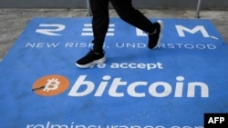 En esta foto de archivo, un hombre pasa junto a una pancarta con el logotipo de bitcoin durante la conferencia sobre criptomonedas Bitcoin 2021 Convention en el Mana Convention Center en Miami, Florida, el 4 de junio de 2021.