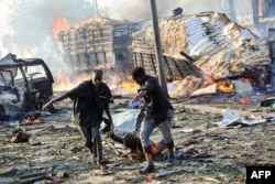 FILE - Two men carry the body of a victim following the explosion of a truck bomb in the center of Mogadishu, Oct. 14, 2017.