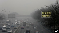 Vehicles drive along a road with a sign reading "Low visibility, slow down" on a heavily polluted day in Beijing, Nov. 30, 2015.