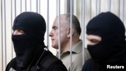 FILE - Oleksiy Pukach, former head of the surveillance department of Ukraine’s Interior Ministry, looks out from a defendant's cage during his trial in the murder of journalist Heorhiy Gongadze, in Kyiv, Ukraine, 29, 2013.