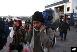 FILE - A man carries his belongings after his arrival along with thousands of other migrants and refugees at the port of Piraeus, near Athens, Dec. 29, 2015.