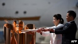 Les triples médaillés d'or olympiques japonais Saori Yoshida (à g.) et Tadahiro Nomura (à d.) avec la flamme olympique à Tokyo, après l'avoir transportée depuis la Grèce. (Photo: Philip FONG / AFP)