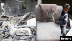A boy holds a chair as he walks on the rubble of damaged buildings after an airstrike on the rebel-held town of Mesraba in the eastern Damascus suburb of Ghouta, Syria, Nov. 26, 2017. 