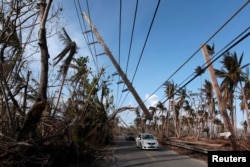 FILE PHOTO: Cars drive under a partially collapsed utility pole, after the island was hit by Hurricane Maria in September, in Naguabo, Puerto Rico, Oct. 20, 2017.