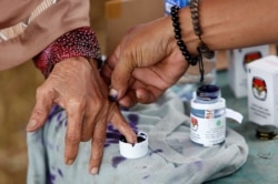 Seorang petugas pemilu membantu seorang perempuan lanjut usia untuk menandai jarinya dengan tinta setelah memberikan suaranya pada Pilkada di Tangerang, Banten, 27 Juni 2018. (Foto: REUTERS/Willy Kurniawan)