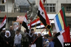 FILE - Residents of the Golan Heights wave Syrian and Druze flags as they gather in front of a portrait of the Syrian President Bashar al-Assad during a protest against the backing of Israel's capture of the Golan Heights by the U.S. president, in the village of Majdal Shams in the Israeli-annexed territory, March 23, 2019.