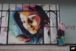 A migrant woman passes graffiti on the wall as she carries supplies at the refugee camp of Ritsona, about 86 kilometers (53 miles) north of Athens, March 14, 2017. More than 60,000 refugees and migrants are stranded in Greece after a series of Balkan border closures and a European Union deal a year ago with Turkey to stop migrant flows.