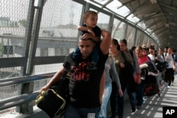 FILE - In this April 29, 2019, photo, Cuban migrants are escorted by Mexican immigration officials in Ciudad Juarez, Mexico, as they cross the Paso del Norte International bridge to be processed as asylum seekers on the U.S. side of the border.