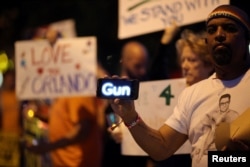 A man holds a scrolling message about guns on his smart phone at a candlelight vigil in West Hollywood, California, following the early morning attacks on a gay night club in Orlando, Florida, June 12, 2016.