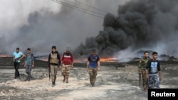 Tribal fighters walk as fire and smoke rises from oil wells, set ablaze by Islamic State militants before IS militants fled the oil-producing region of Qayyara, Iraq, Nov. 1, 2016.