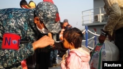 A Bangladesh navy personnel helps a child to wear a mask due to ongoing coronavirus disease (COVID-19) before getting on board a ship to move to Bhasan Char island in Chattogram, Bangladesh, Dec. 29, 2020.