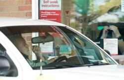 Pharmacy workers give instruction on how to administer a COVID-19 nasal swab self-exam at a drive-up CVS pharmacy in Dallas, Sept. 18, 2020.