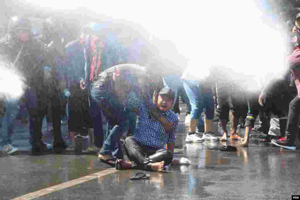 A protester is helped by a fellow protester at a rally against Myanmar&#39;s military coup in Mandalay as riot police use water cannons to disperse demonstrators, Feb. 9, 2021. (Credit: VOA Burmese Service)