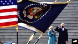 President Joe Biden salutes as his wife, Jill, puts her hand over her heart as they review the troops from the steps of the US Capitol during the inauguration, Jan. 20, 2021, in Washington. 