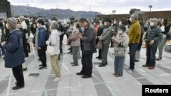 People wearing protective face masks form a line while keeping distance from others as they try to watch the Olympic flame during the Tokyo 2020 Olympics Flame of Recovery tour in Ofunato, March 23, 2020. (Kyodo/via Reuters)