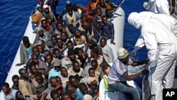 Migrants crowded in an inflatable dinghy await rescue by the Italian coast guard’s vessel Denaro off the Libyan coast, in the Mediterranean Sea, April 22, 2015. 