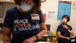 Carol Kelly, right, waits to receive a Moderna variant vaccine shot at Emory University's Hope Clinic, March 31, 2021, in Decatur, Ga. Kelly was the first person to receive a shot in this new clinical trial.