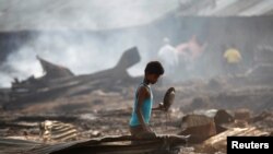 Seorang anak laki2 mencari barang-barang yang dianggap masih berguna di antara benda-benda yang hangus terbakar setelah kebakaran memporak porandakan kamp penampungan pengungsi Rohingya di dekat Siitwe, Myanmar (3/5). 