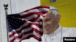 FILE - The U.S. flag flies in front of a mural of Pope Francis on the side of a building in midtown Manhattan in New York, Aug. 28, 2015.
