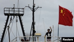 Captain Why Yang of Hong Kong fishing vessel "Kai Fung No.2" waves next to a Chinese national flag as he reaches in Hong Kong's island of Cheung Chau, August 22, 2012. 