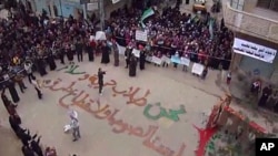 In this image from amateur video made available by the Shaam News Network and shot on Friday, December 30, 2011, protesters gather in Homs, Syria. The writing on the ground, in Arabic, reads: "We are those who seek freedom and peace. We are not thieves or