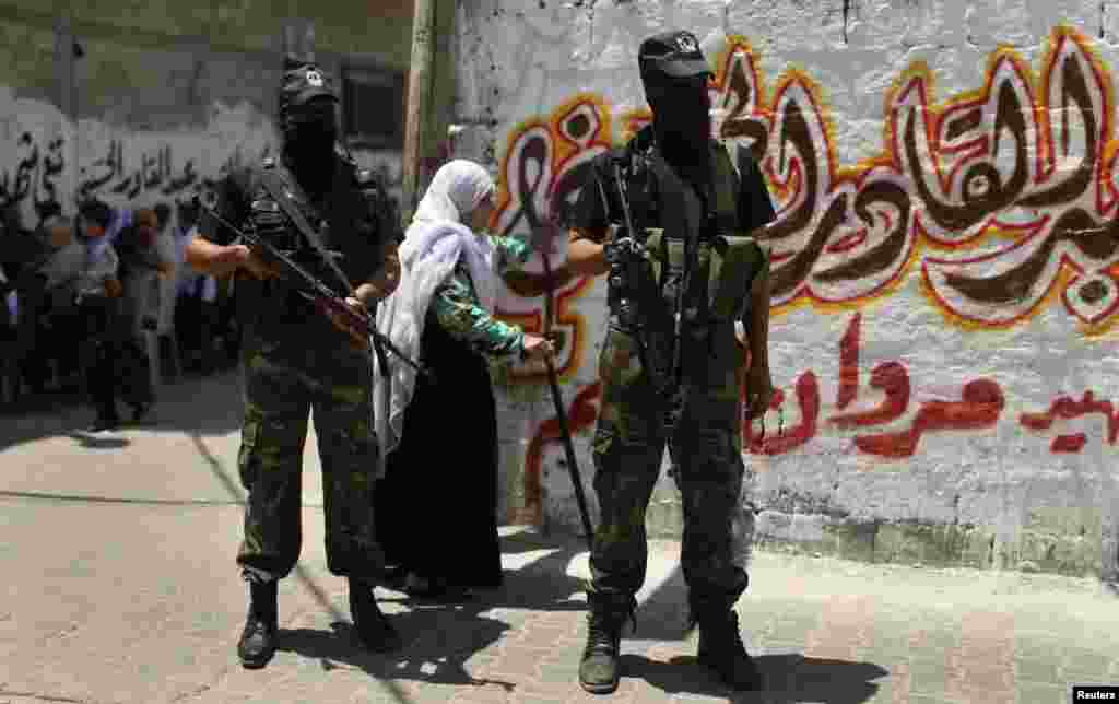 A woman walks behind Palestinian militants standing guard during the funeral of their comrade Marwan Sleem in the central Gaza Strip, July 7, 2014. 