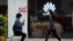 A woman wearing a face mask to help curb the spread of the coronavirus browses her smartphone as a masked woman walks by the Huawei retail shop promoting it 5G network in Beijing Oct. 11, 2020.