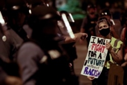 FILE - A protester confronts a line of police in riot gear after a unity march to protest police brutality, in Kansas City, Mo., June 4, 2020.
