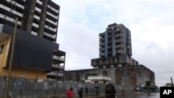 People walk past buildings damaged or unfinished as a result of Liberia's decade-and-a-half long civil war. In the post-war era, health officials are stepping up the fight against leprosy.