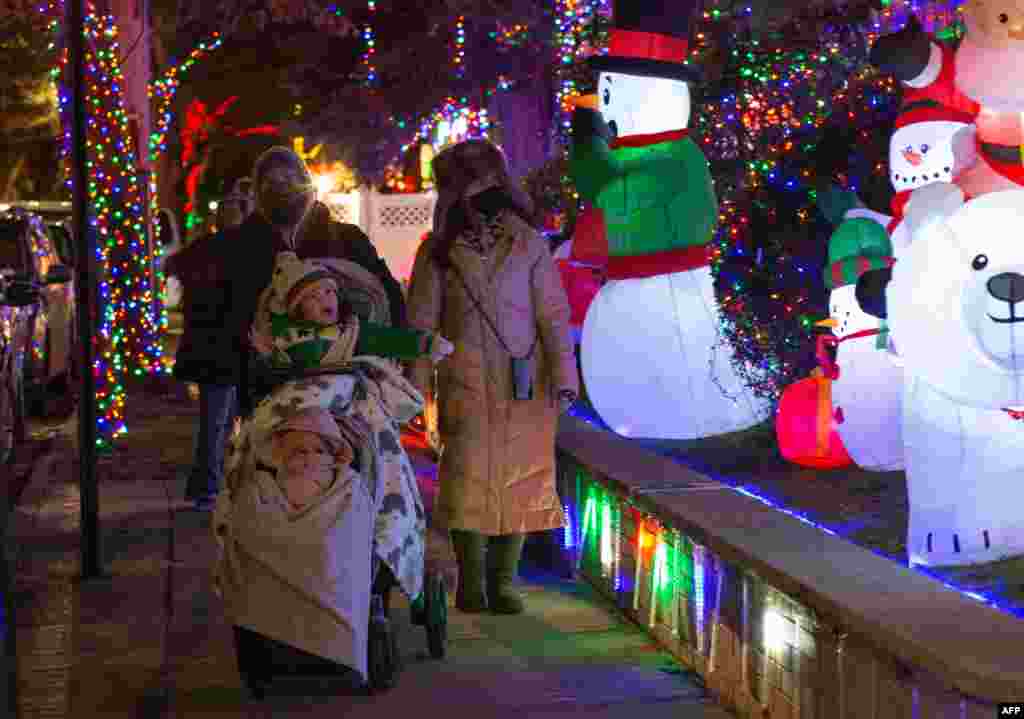 Una familia mira casas decoradas para Navidad en el barrio de Dyker Heights de Brooklyn, el 15 de diciembre de 2020 en la ciudad de Nueva York. [AFP]