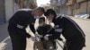 Des agents de santé aident un homme en fauteuil roulant à enfiler ses gants pour empêcher la propagation du coronavirus à Qamishli, Syrie, le 23 mars 2020.