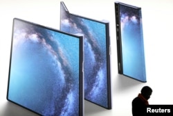 A man checks his phone next to an advertisement of a new Huawei Mate X device at the Mobile World Congress in Barcelona, Spain, Feb. 26, 2019.