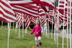 Hazel Roberts walks in a field of flags ahead of Memorial Day, Saturday, May 23, 2020, in Cohasset, Mass. (AP Photo/Michael Dwyer)